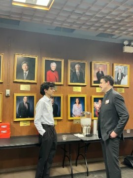 A student talking with a professional in front of a wall of framed portraits